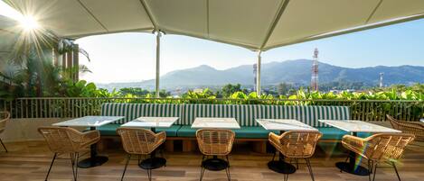 An outdoor seating area with tables and chairs, a green sofa, and a view of mountains.