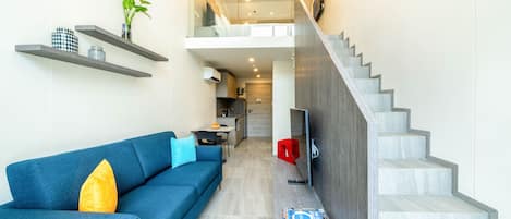 Una sala de estar moderna con un sofá azul, una escalera y una cocina al fondo.