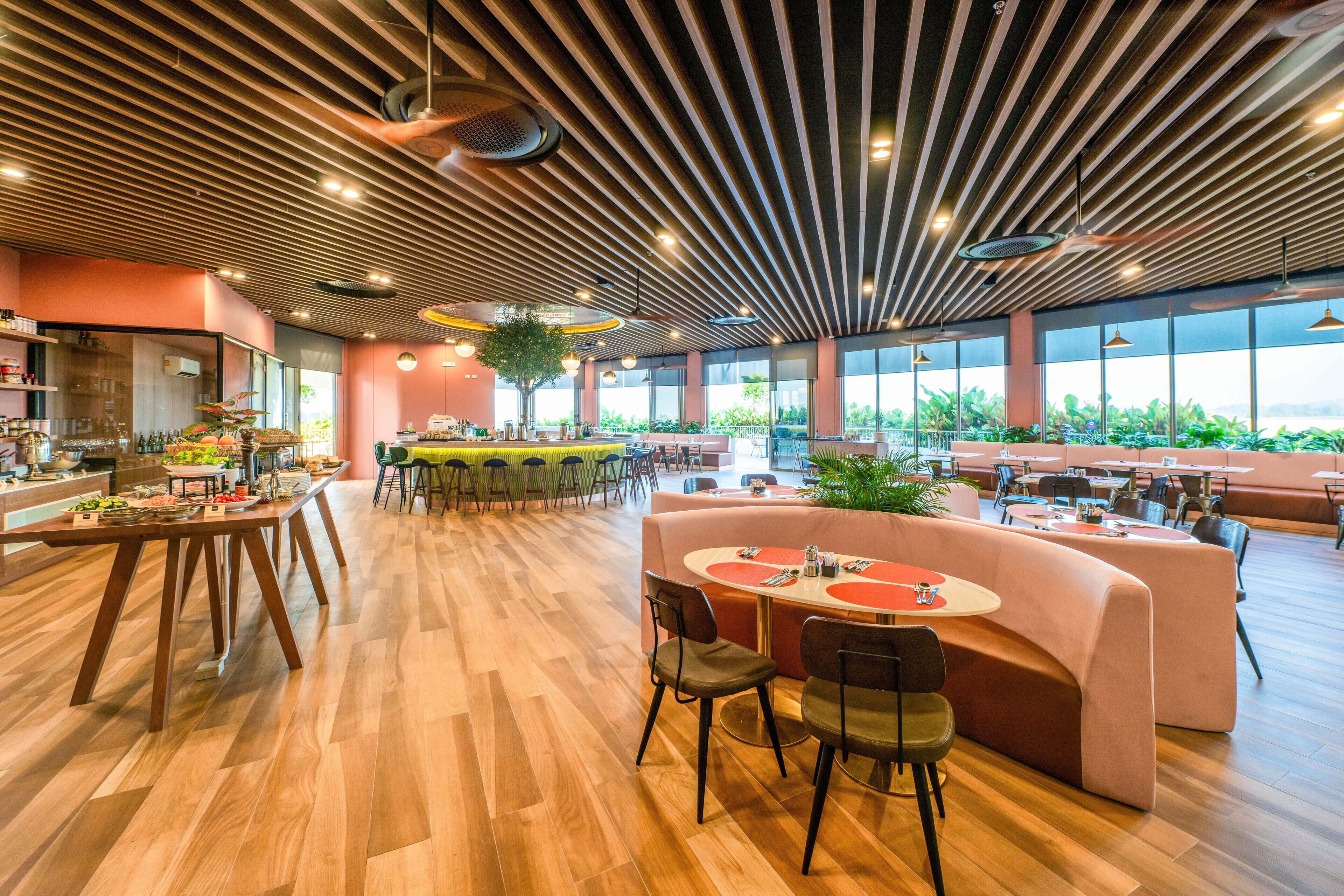 Un restaurant spacieux doté d’un plancher en bois, d’un îlot central avec des sièges et de grandes fenêtres offrant une vue sur la verdure.