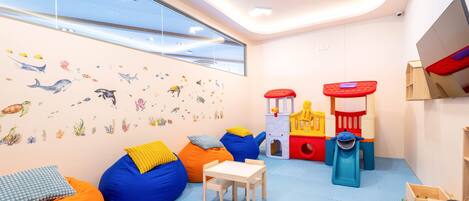 A children's playroom with bean bags, a playhouse, and a window with a view.