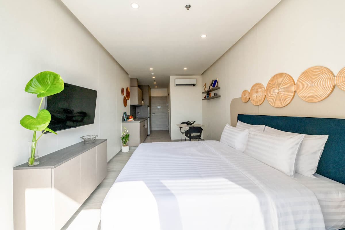 Une chambre d’hôtel moderne dotée d’un grand lit, d’un téléviseur fixé au mur, d’un petit coin cuisine et d’une table à manger.