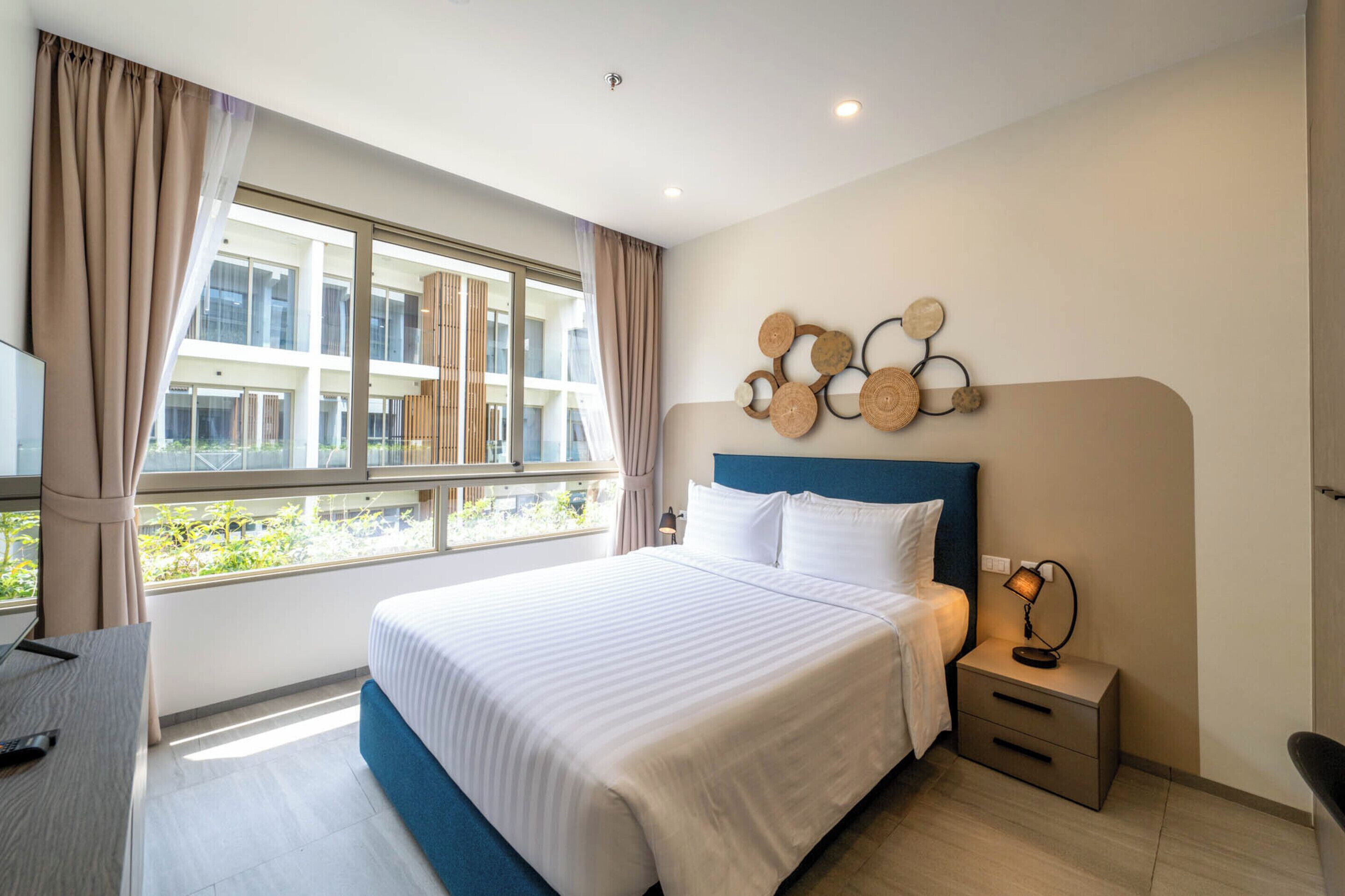 A modern hotel room with a large bed, a desk, and a window with curtains.