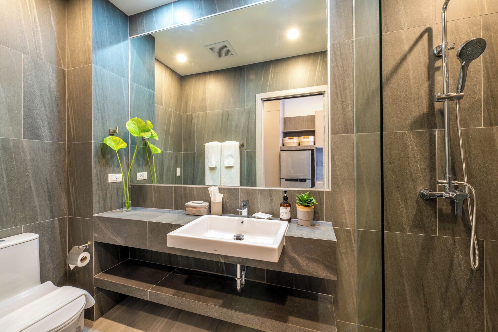 A modern bathroom with a white sink, a mirror, a shower, and a toilet.