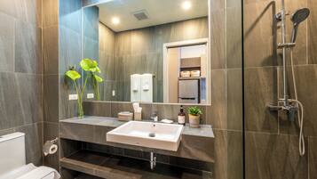 A modern bathroom with a white sink, a mirror, a shower, and a toilet.