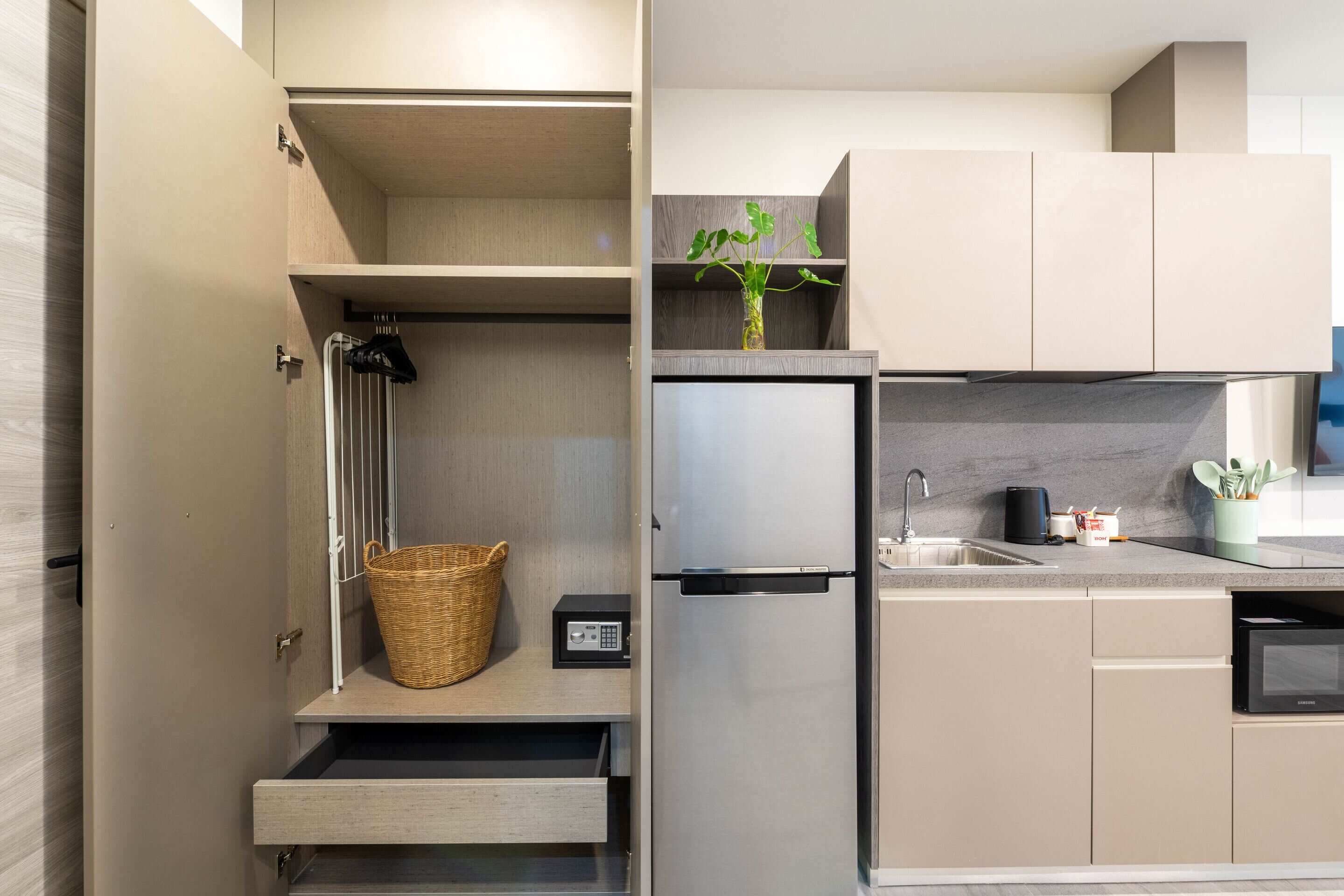 A modern kitchen with a built-in refrigerator, a microwave, and a sink. There is a basket on the countertop and a small plant on the shelf.