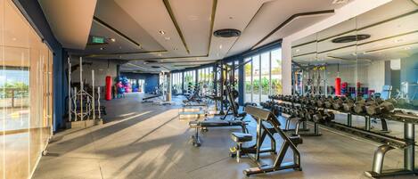A modern gym with various exercise equipment, large windows, and a clean, spacious layout.