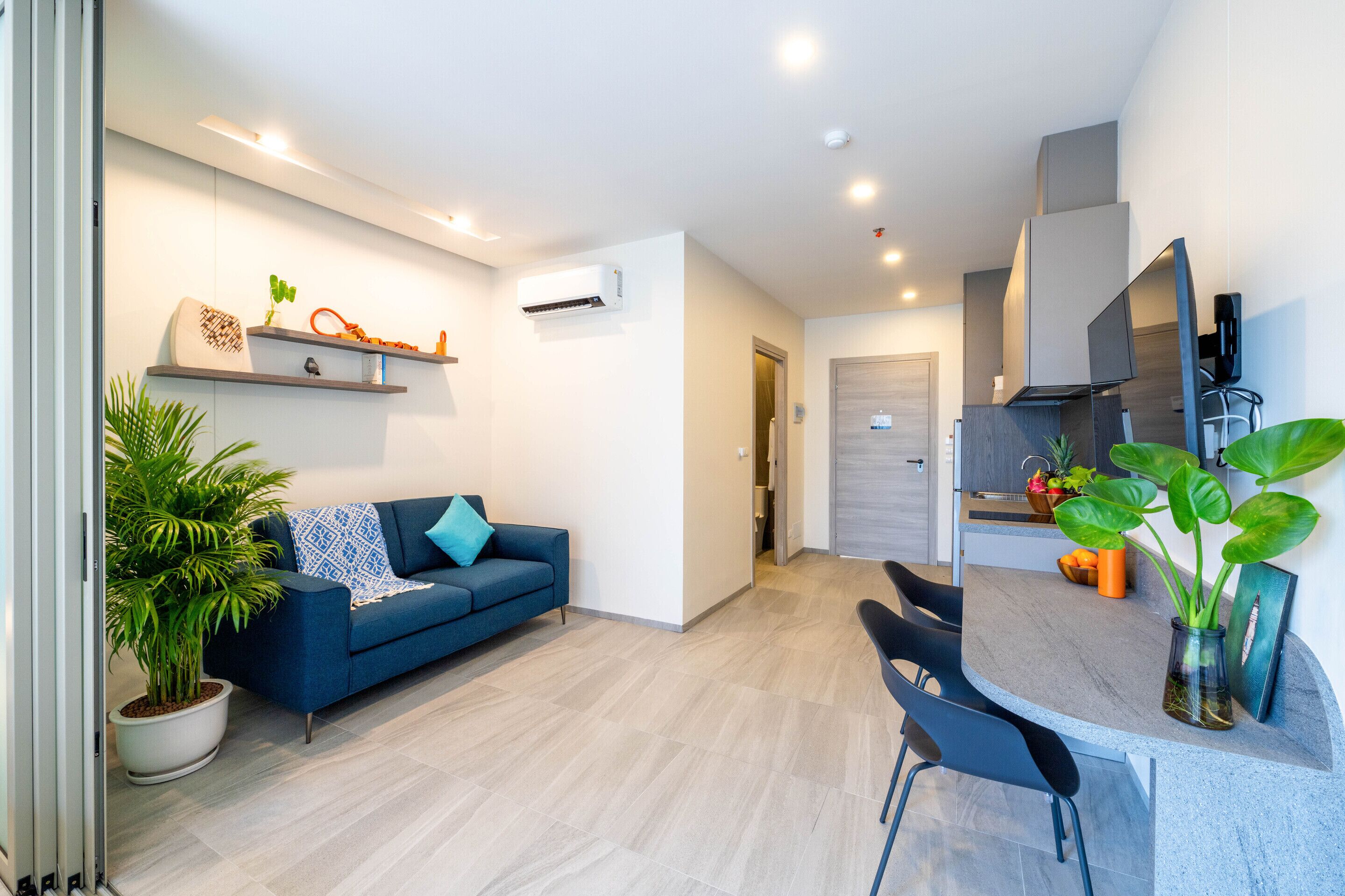 A modern living room with a blue sofa, a dining area with a table and chairs, and a kitchen in the background.
