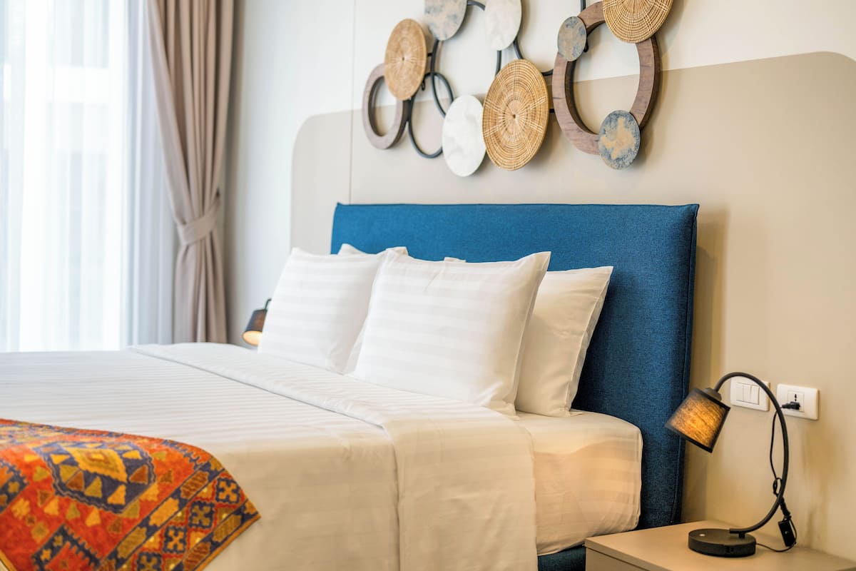 Un lit bien fait, avec du linge de lit blanc et une tête de lit bleue, une lampe de chevet et une décoration murale composée de motifs circulaires et ovales.