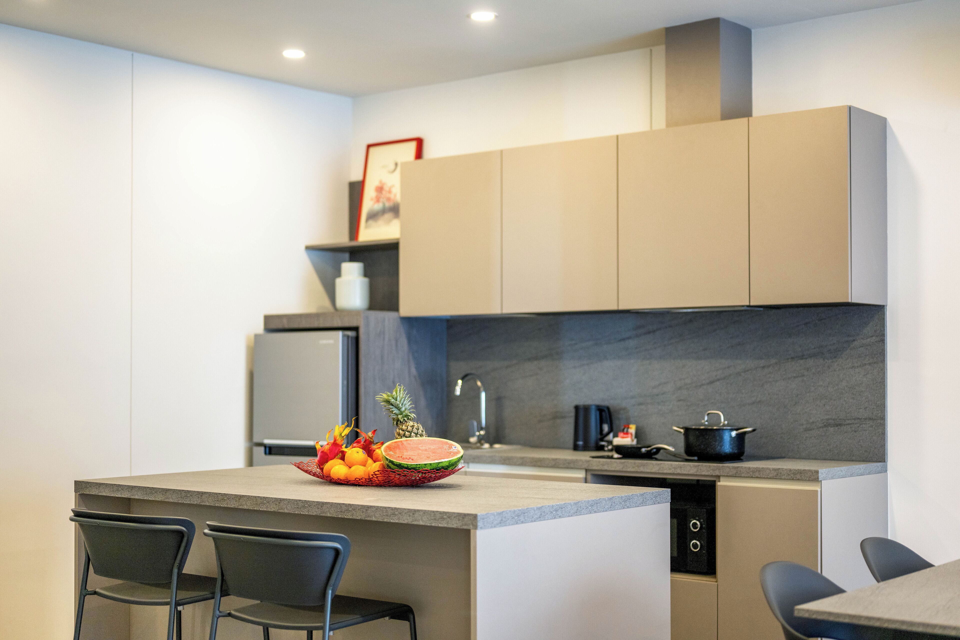 Una cocina moderna con una isla central, dos taburetes de bar, un refrigerador y un microondas.
