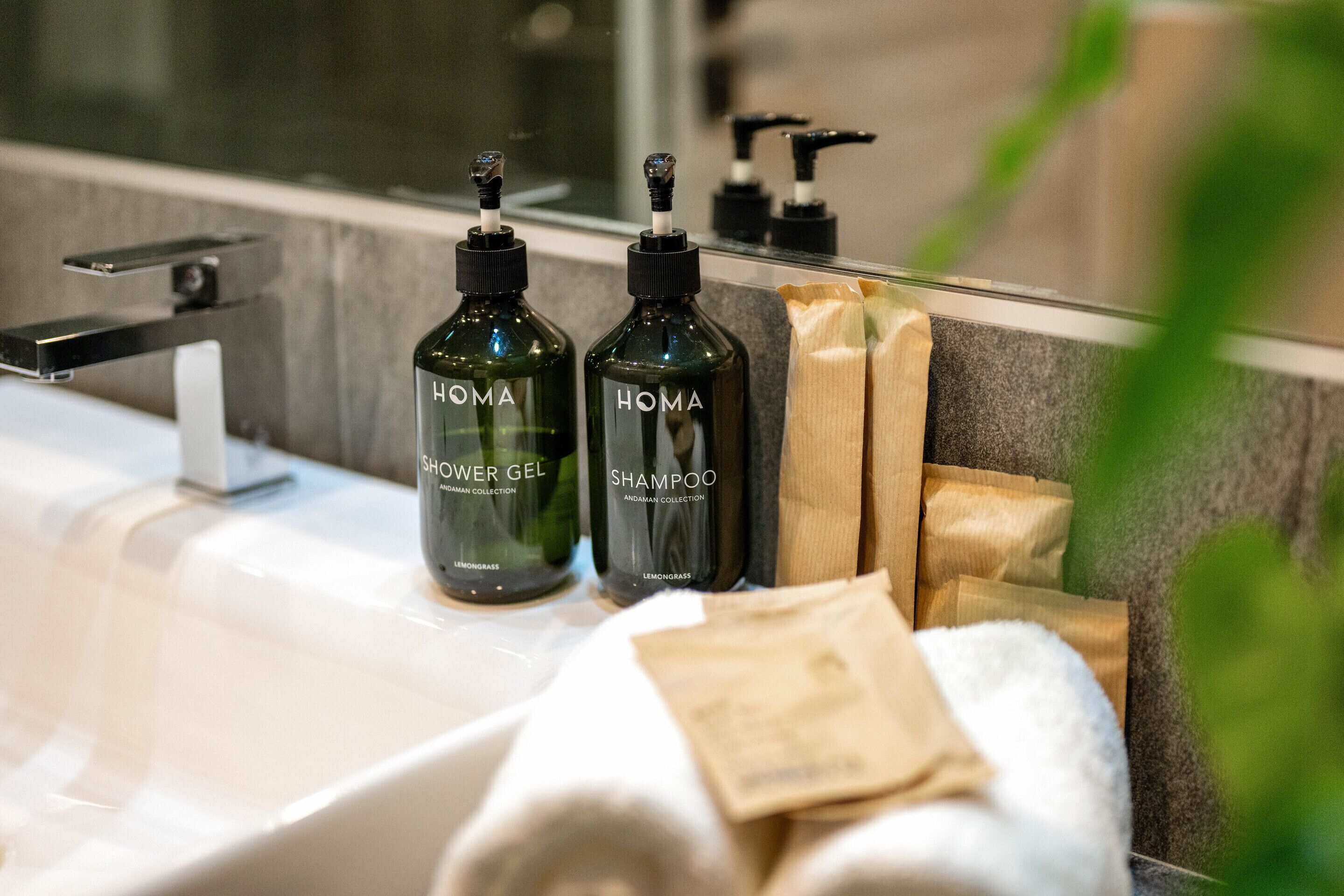 Un bagno con un moderno lavandino, due flaconi di bagnoschiuma e shampoo HOMA e un asciugamano.