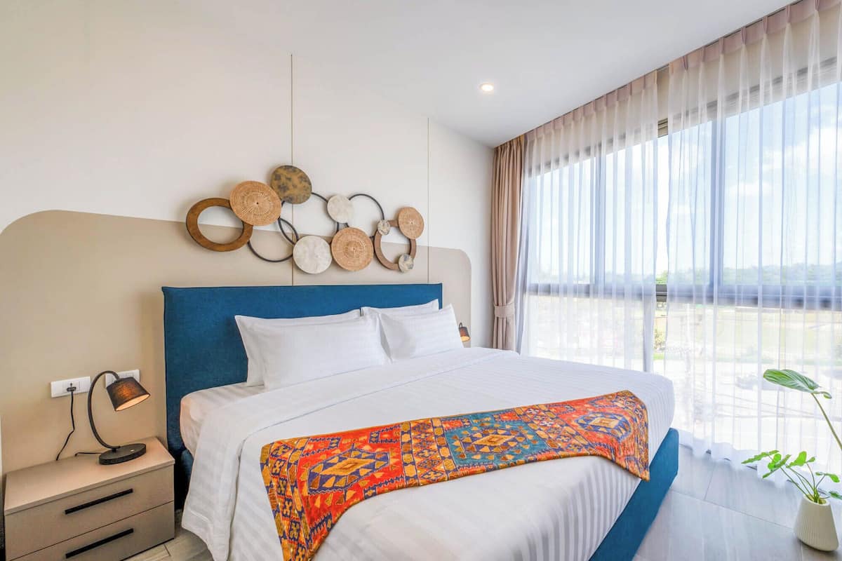 Une chambre d’hôtel avec un grand lit, une table de chevet, une lampe, un élément décoratif mural et une vue sur l’extérieur.
