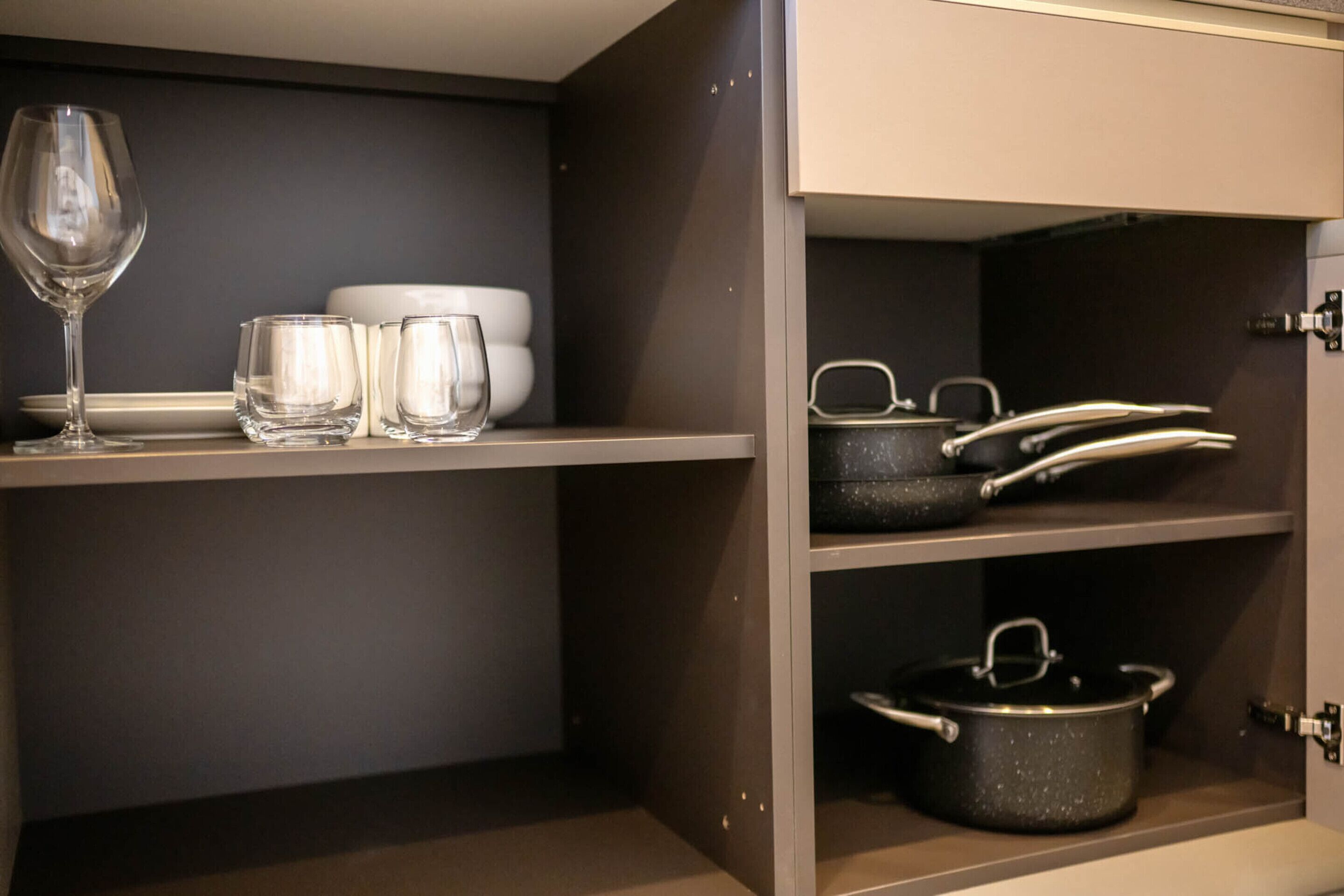 A kitchen with shelves holding wine glasses, bowls, and cookware.