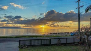 Un coucher de soleil sur une étendue d’eau, avec une route au premier plan et une clôture.