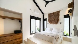 Une chambre à coucher moderne avec un lit, une commode en bois, un ventilateur de plafond et de grandes fenêtres.
