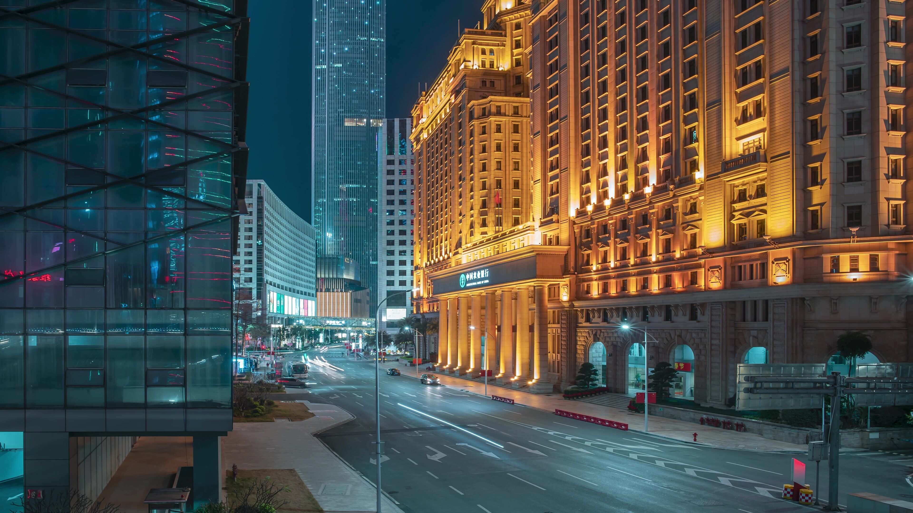 Un hotel moderno con una entrada imponente, fachada bien iluminada y una calle concurrida al fondo.