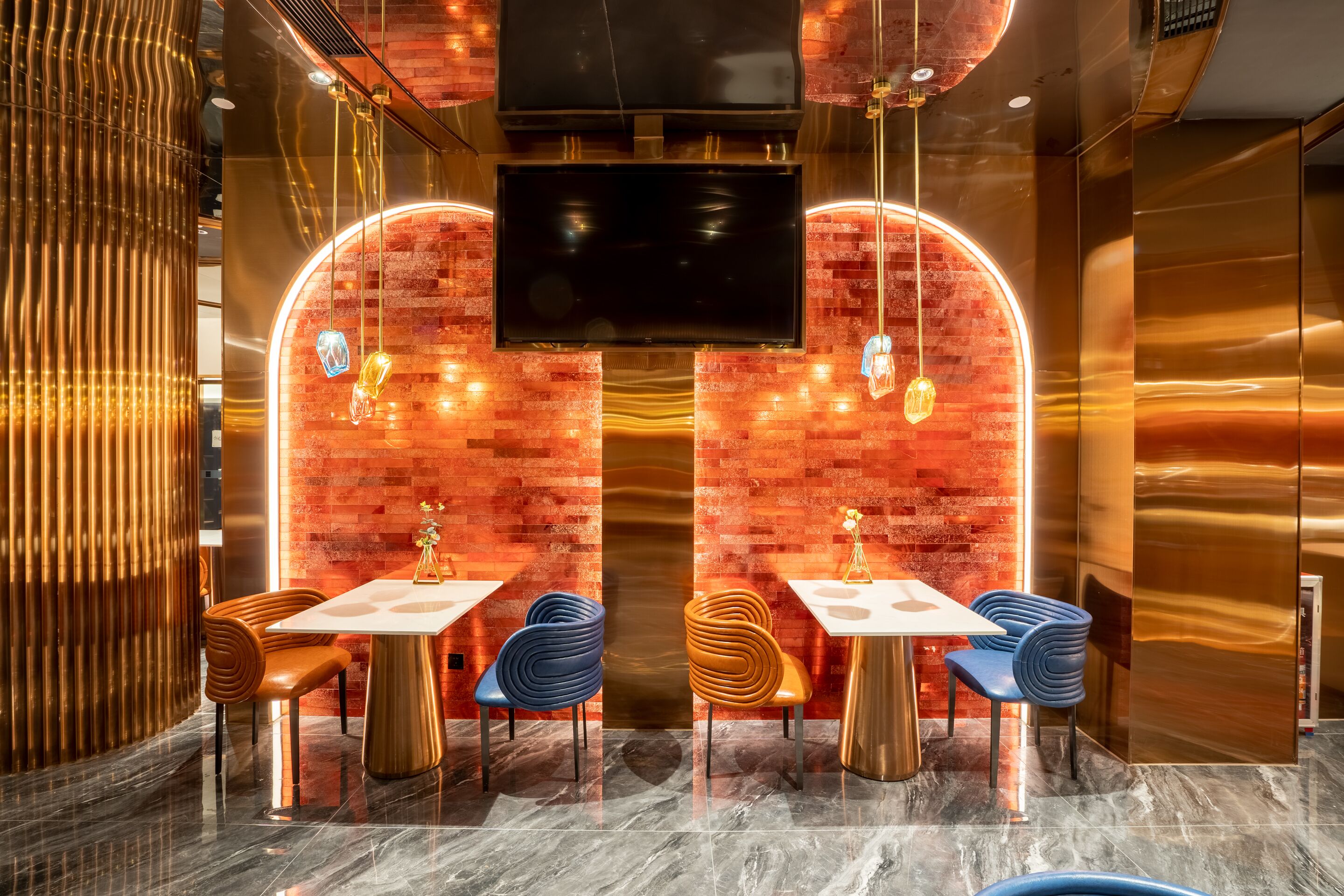 A modern restaurant interior with brick walls, a TV screen, and uniquely designed chairs.