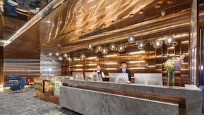 Una moderna zona de recepción con mostrador de mármol, dos recepcionistas y un jarrón decorativo con flores.