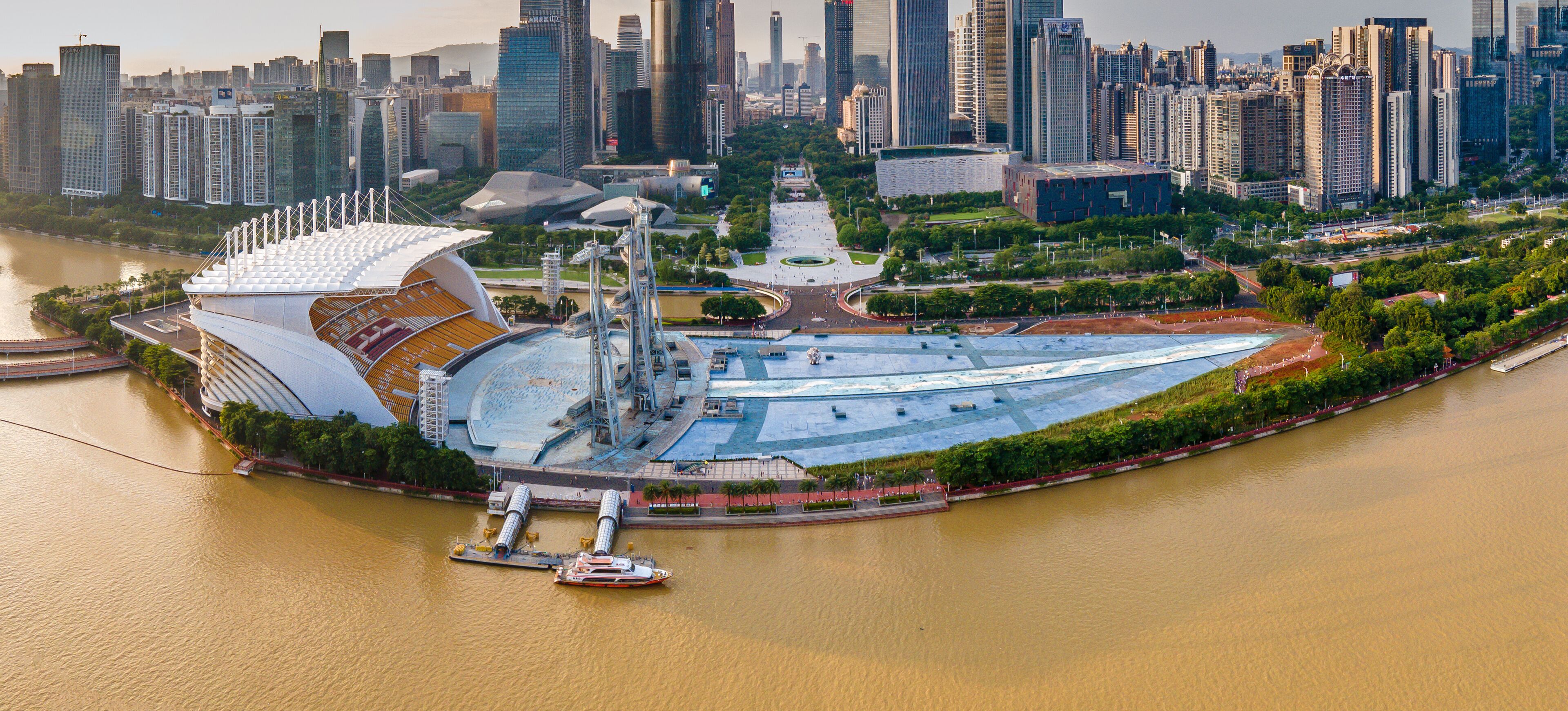 A modern architectural complex with a large stadium, a river, and surrounding high-rise buildings.