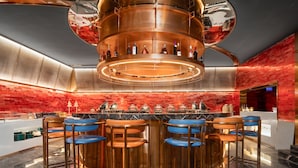 Un bar moderno con una barra circular central, varios taburetes y una pared de ladrillo rojo.