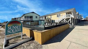 A beachfront property with a sign reading "Sunset Square," featuring a wooden deck, a pool, and a two-story building with a balcony. - Sunset Square O - Second Row complex in Garden City Beach, SC (Garden City)