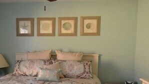 A bedroom with a bed, pillows, a nightstand, a lamp, and four framed pictures on the wall. - Sunset Square O - Second Row complex in Garden City Beach, SC (Garden City)