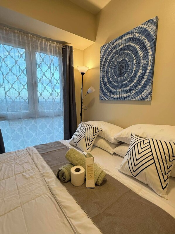 A hotel room with a bed, pillows, a lamp, and a painting on the wall.