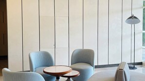 Un espacio lounge moderno con sillones tapizados en azul claro, una mesa redonda y una lámpara de pie.