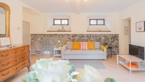 A modern living room with a stone wall, a sofa with cushions, a TV stand, a wooden dresser, and a large mirror. - La Piazza di Cernobbio (Cernobbio)