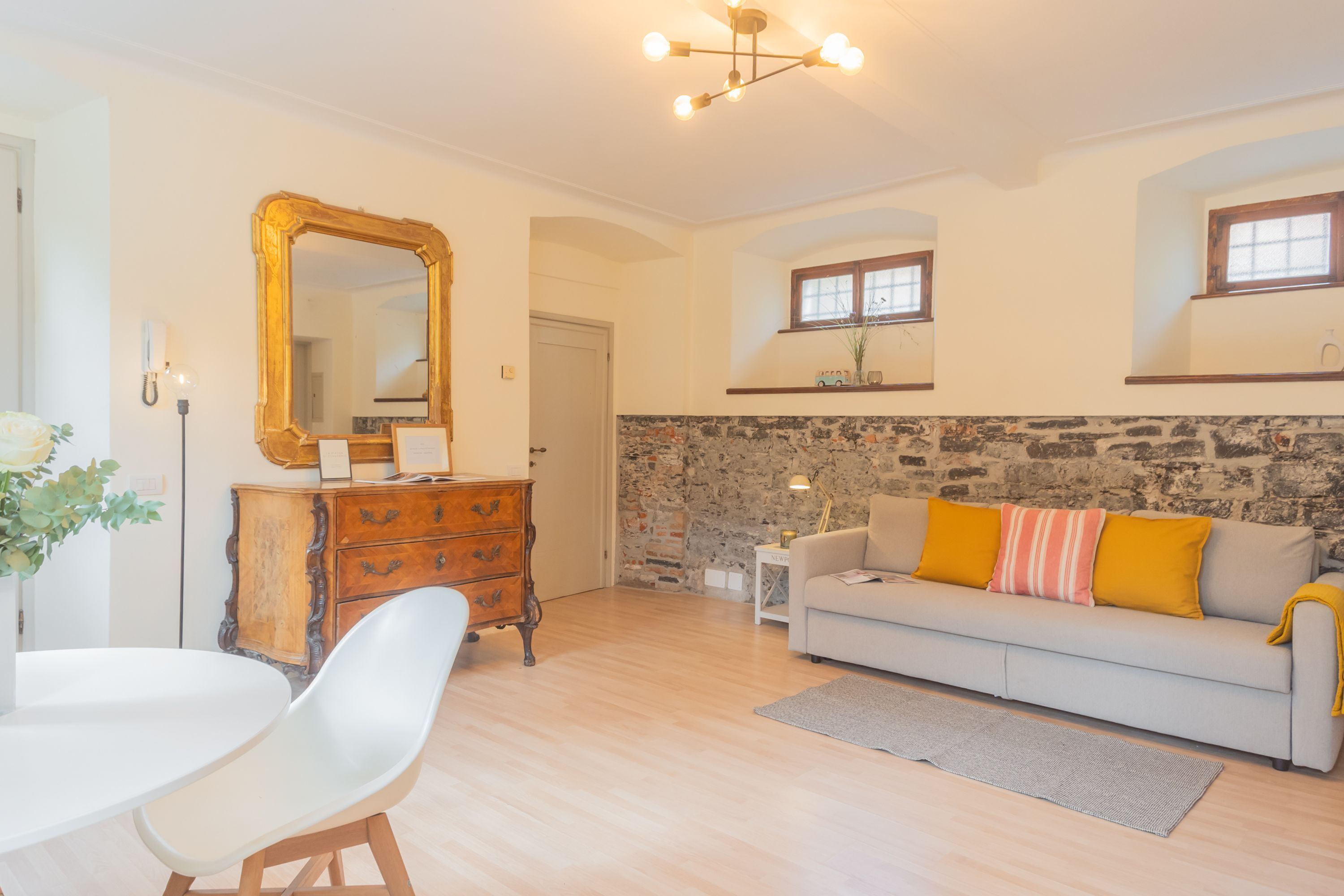 A living room with a stone wall, a sofa with yellow cushions, a white table with chairs, and a wooden dresser.