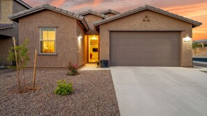 A single-story house with a garage, a small front yard with gravel and plants, and a sunset sky.