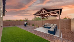 A backyard with a covered patio, a barbecue grill, and a lawn.