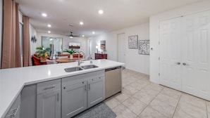 A modern kitchen with a central island, a dining area with a red sofa, and a white door.