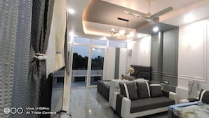 Un salon moderne avec un canapé, une table basse et un ventilateur de plafond. Il y a un balcon avec vue sur les arbres.