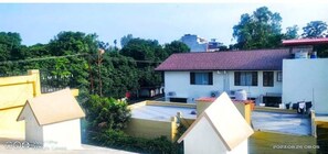 Residential area with a white building featuring a red-tiled roof, surrounded by lush greenery and other structures.