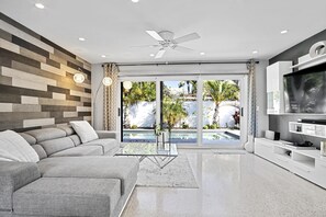 Uma sala de estar moderna com um sofá seccional cinza, uma mesa de centro de vidro e uma TV de tela plana na parede.