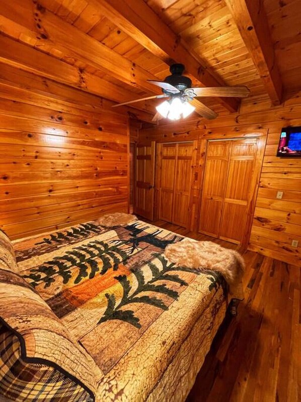 Une chambre dans une cabane en bois, avec un lit, un ventilateur de plafond et un téléviseur fixé au mur.