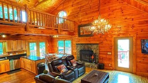 A spacious living room with a fireplace, leather sofas, and a high ceiling with exposed beams. - Smokey Mountain Retreat (Waynesville)