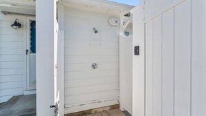 Fachada blanca de un edificio con una puerta, un ventanal pequeño y una rejilla metálica en la pared.