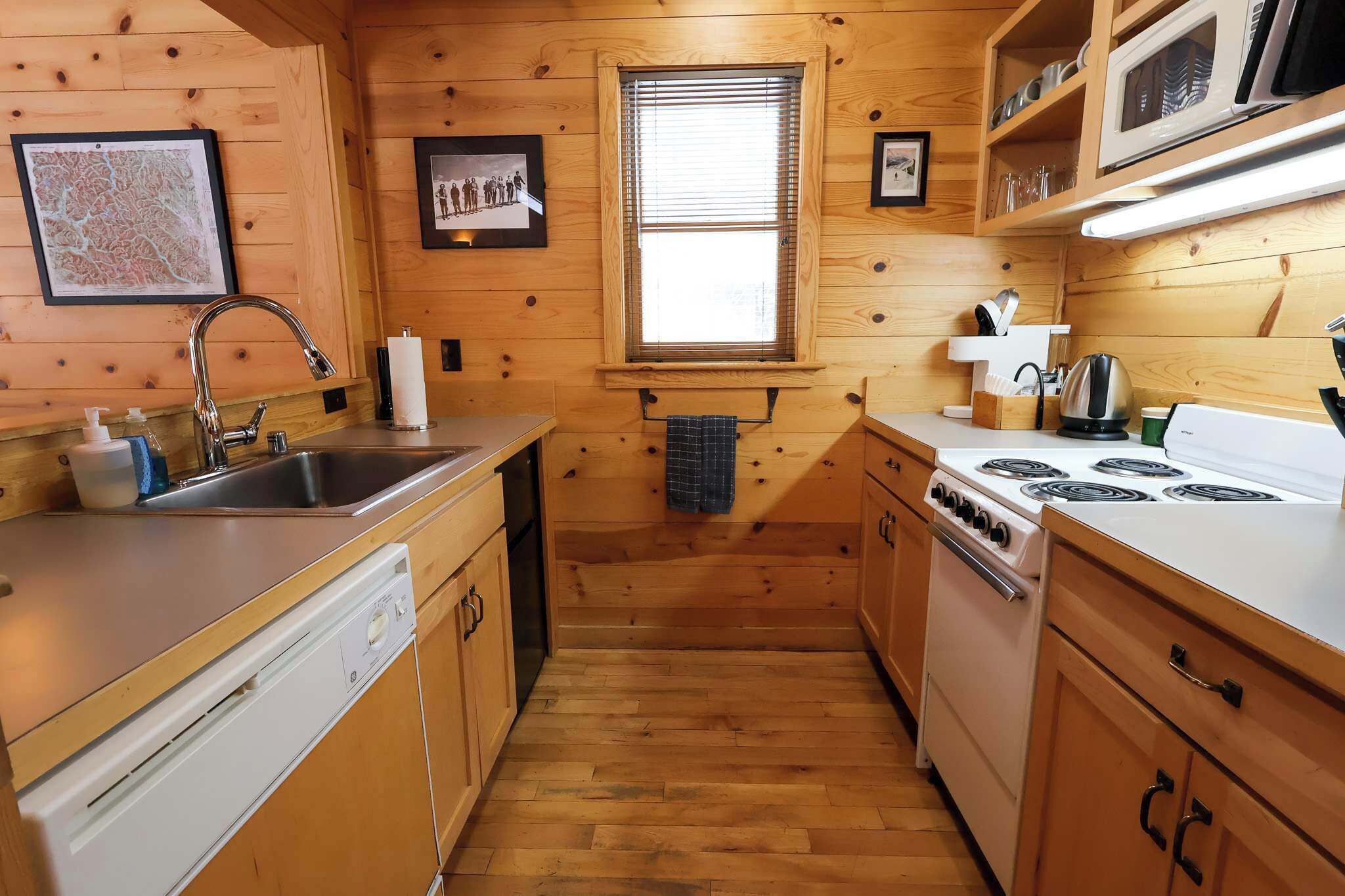 A wooden cabin-style kitchen with a sink, stove, and microwave.