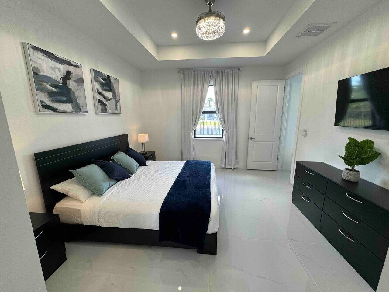 Un dormitorio moderno con cama, mesitas de noche, cómoda, televisor y obras de arte en las paredes.