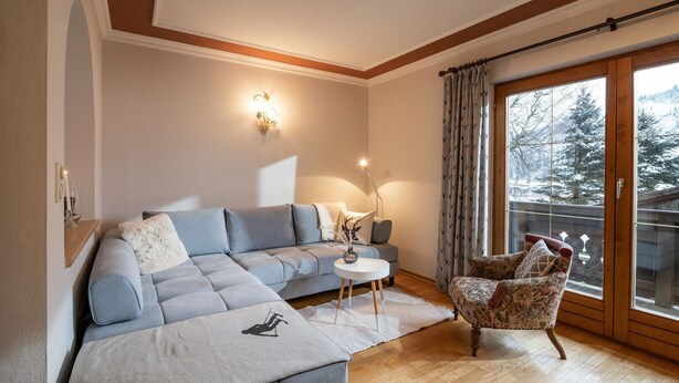 Un salon moderne avec un canapé d’angle, une petite table ronde et un fauteuil à motifs floraux.