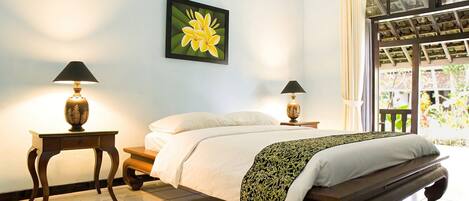 A bedroom with a bed, two bedside tables with lamps, a large window with curtains, and a wall-mounted picture of a flower.