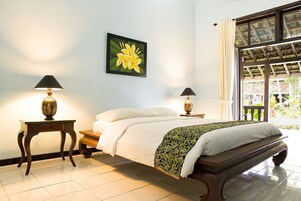 Un dormitorio con cama, dos mesitas de noche con lámparas, un ventanal con cortinas y un cuadro de una flor colgado en la pared.