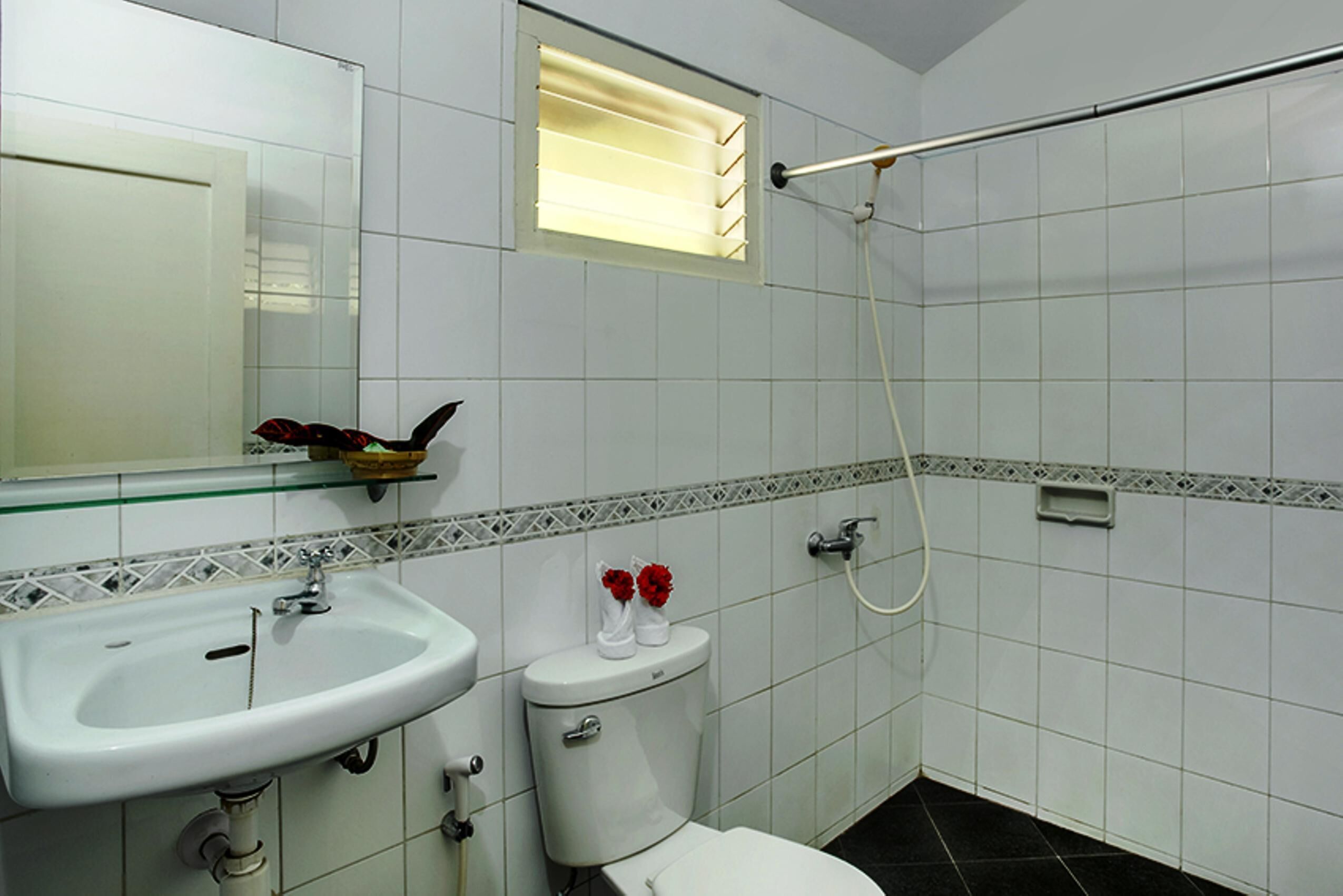 A bathroom with a white sink, toilet, and shower. There is a mirror above the sink and a small window above the toilet.
