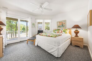 A bedroom with a bed, a chair, a nightstand, a lamp, a ceiling fan, and a window with a view of trees.