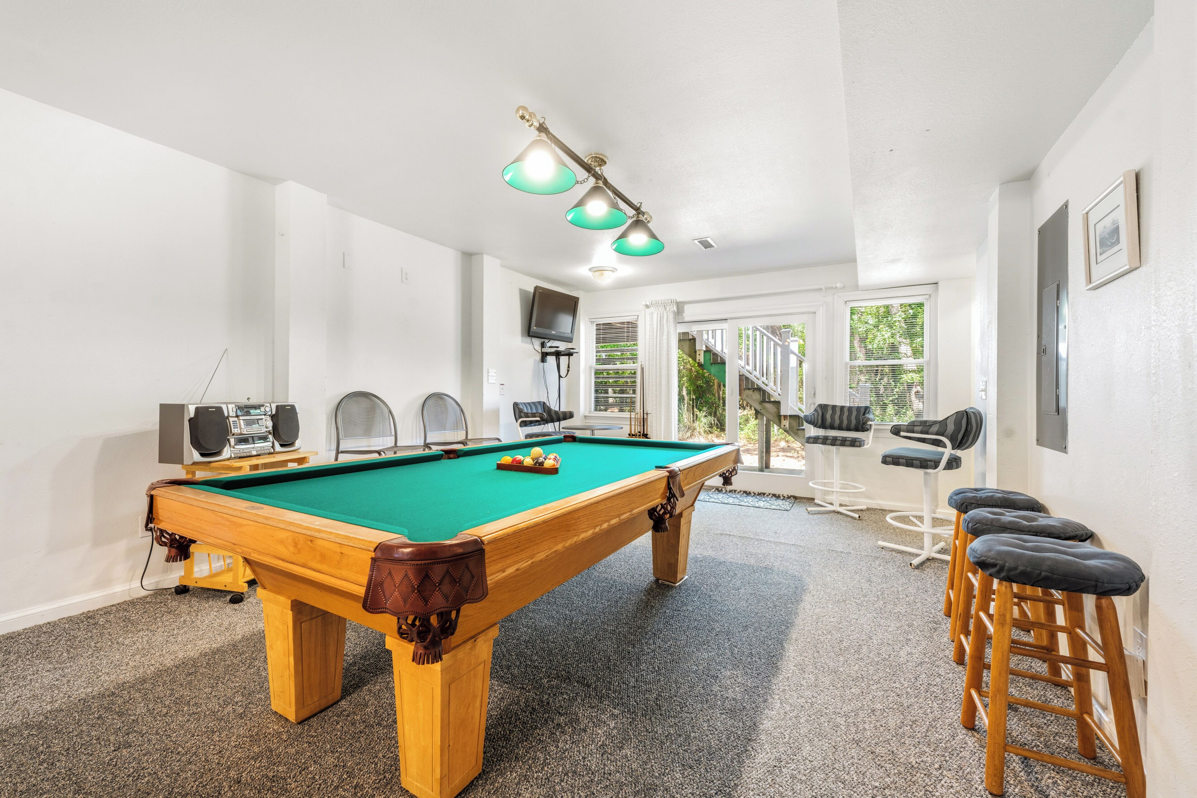 A pool table with speakers, a bar area, and a view to the outside.