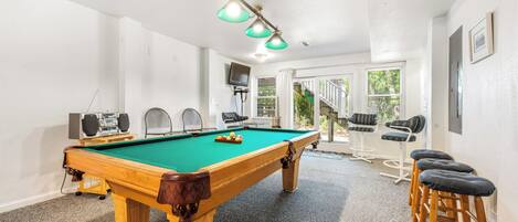 A pool table with speakers, a bar area, and a view to the outside.