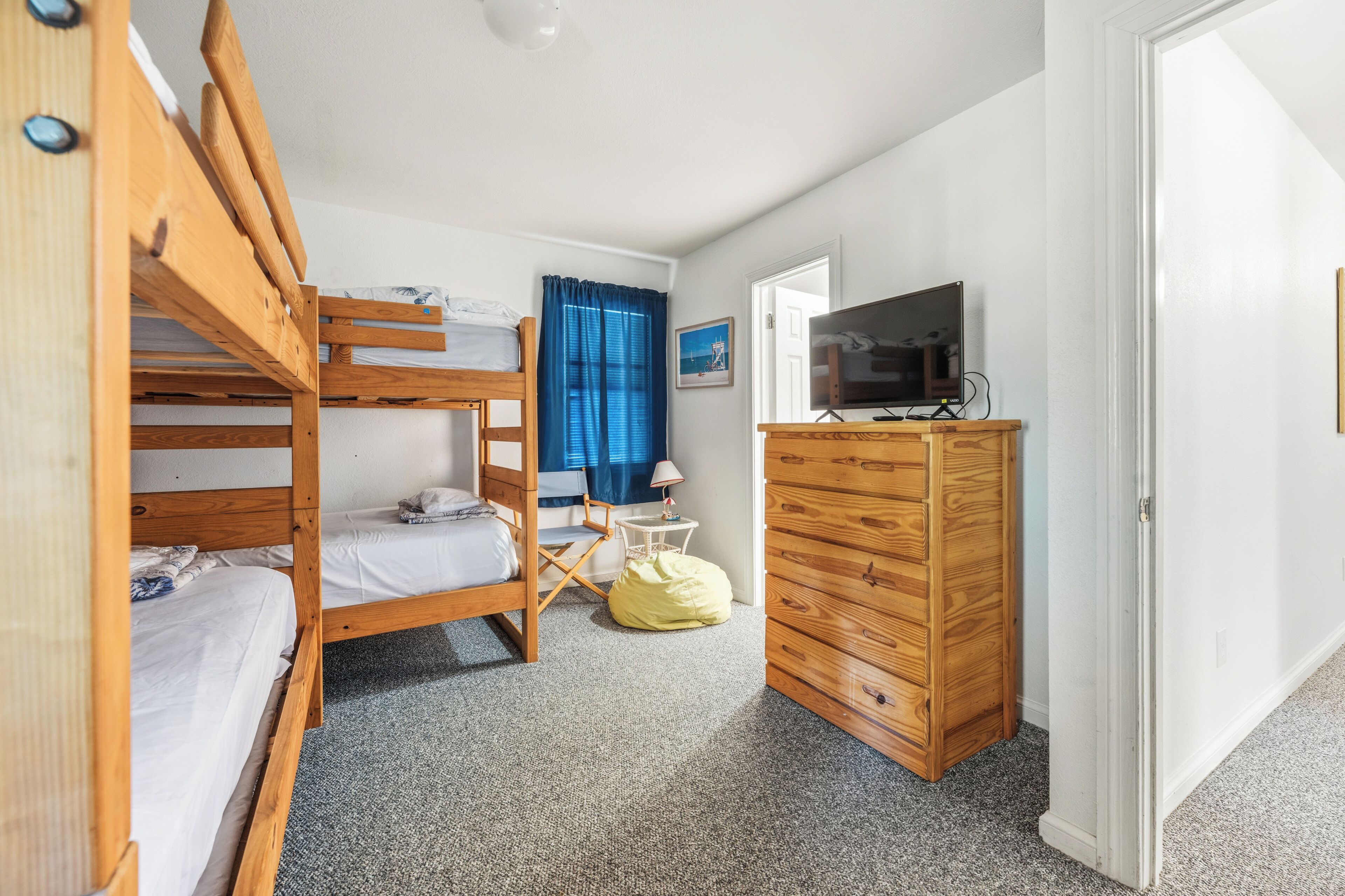 A bunk bed room with a television, a dresser, and a small table with a lamp.