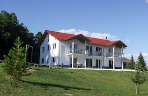 A two-story house with a red roof, a balcony, and a grassy yard.