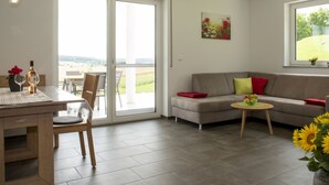 Una sala de estar moderna con comedor, un sofá, una mesita y vistas a través de un ventanal.